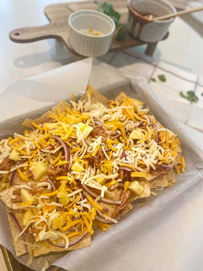 layer cheese on a pan of hawaiian chicken nachos