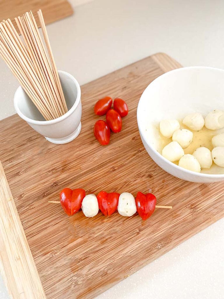 valentines caprese skewer on a board with mozzarella, tomatoes and skewers