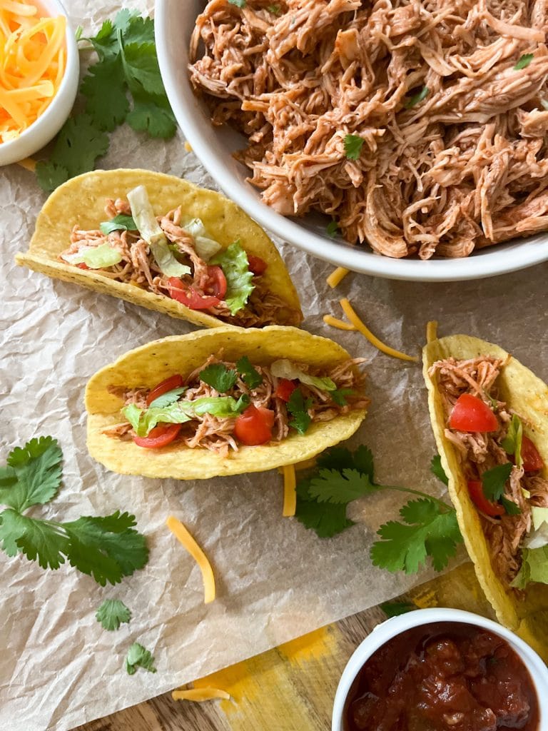 3 ingredient slow cooker mexican shredded chicken in bowl with 3 tacos