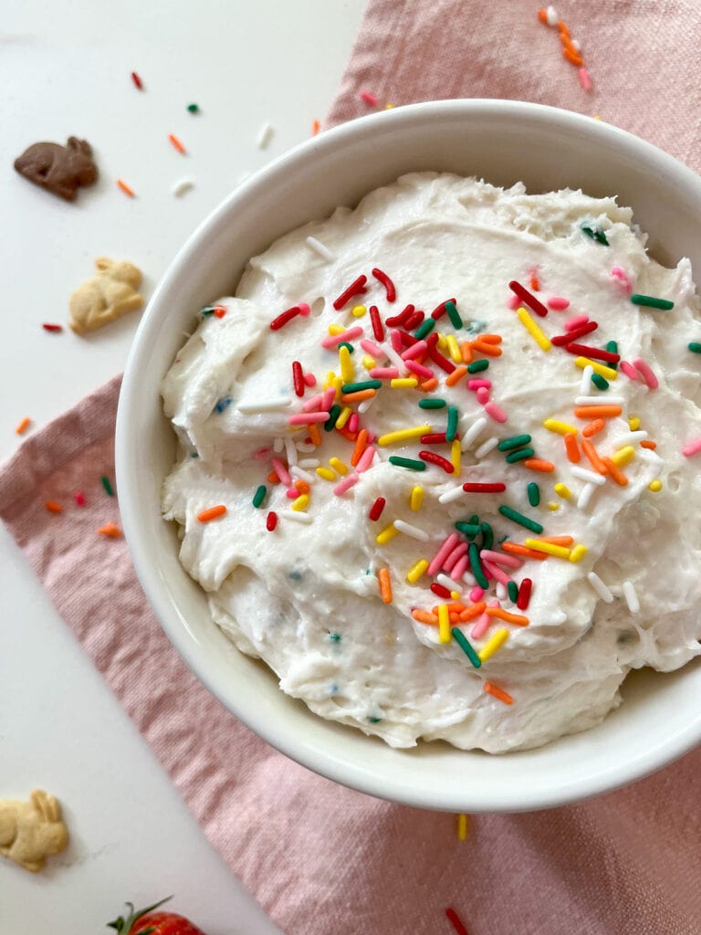 Funfetti Cake Dip in a bowl topped with rainbow sprinkles and bunny cookies on the side