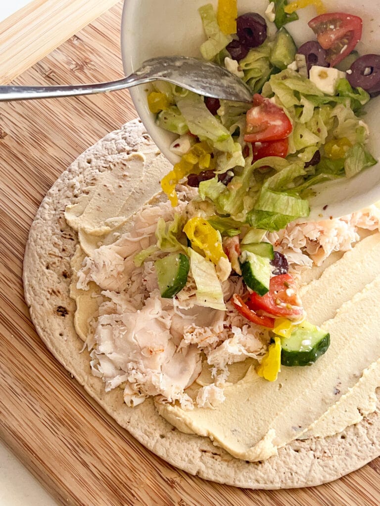 pour salad mixture on top of hummus for Greek Turkey Wraps with Hummus