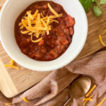 Chili with Tomato Juice in a bowl with shredded cheese and a spoon