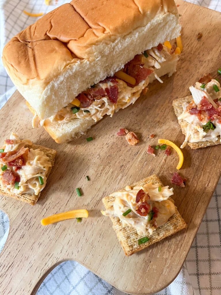 Slow Cooker Creamy Ranch Chicken With Bacons served on a roll and on crackers on a wooden tray