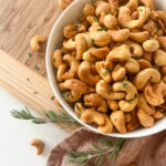 Sweet Heat Roasted Rosemary Cashews in a bowl in a wooden background with extra sprigs of rosemary