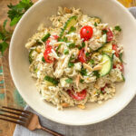 Mediterranean Chicken and Rice Salad in a white bowl on wood background with grey napkin and bronze fork