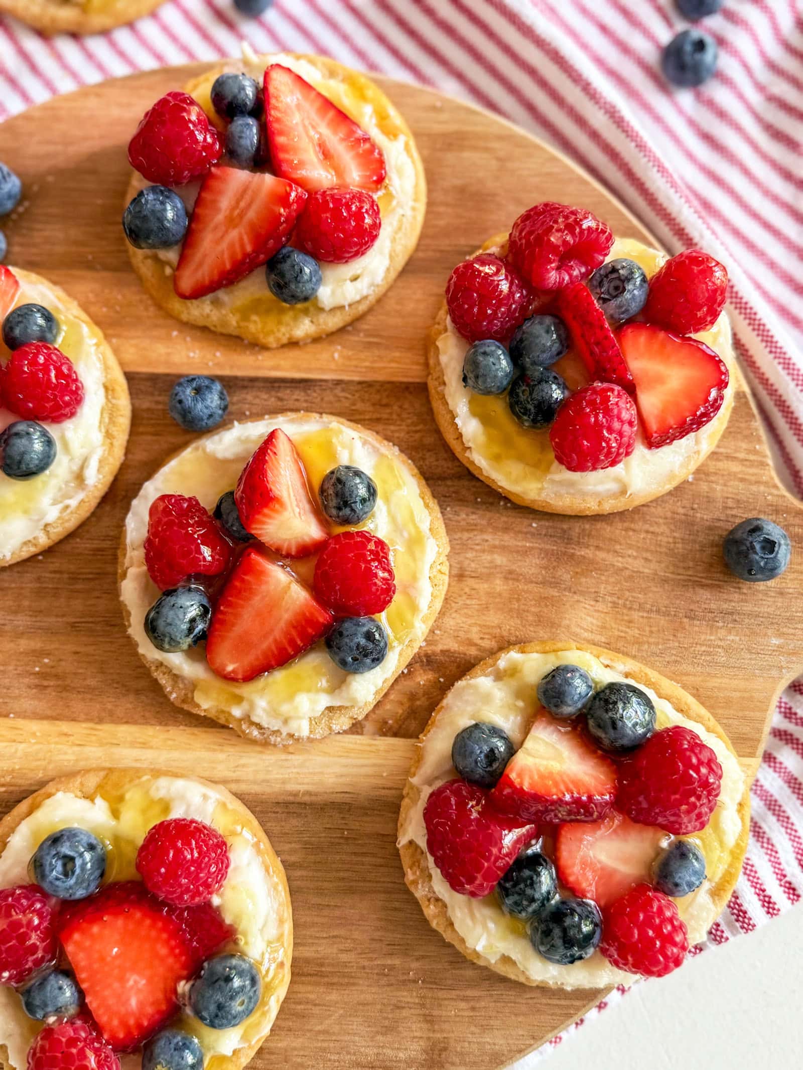 (Red, White & Blue) Mini Sugar Cookie Fruit Pizzas on a wood tray with a red and white striped towel