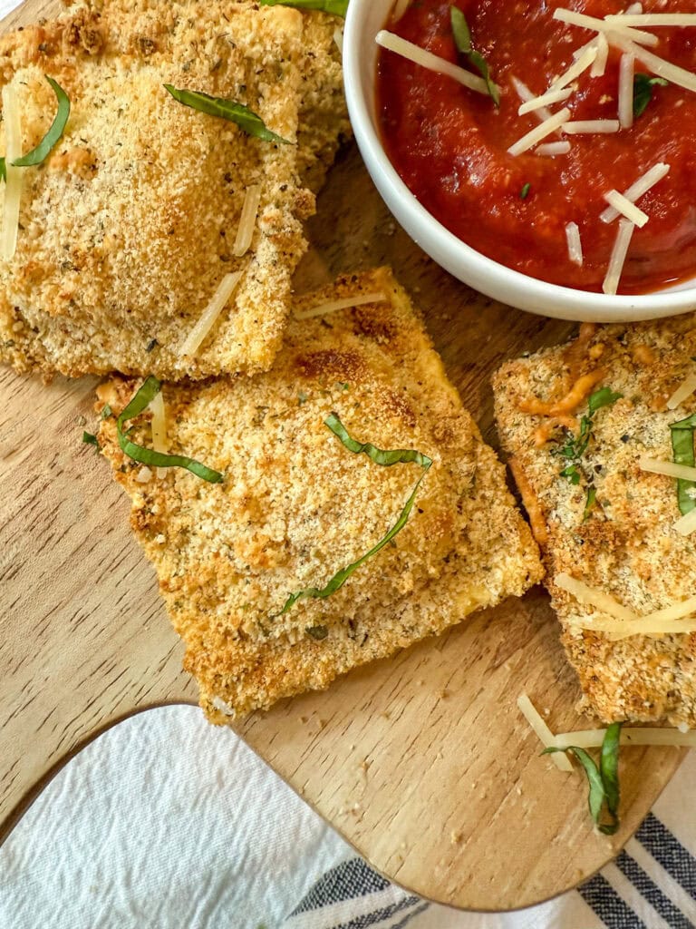 air fryer toasted ravioli on a wood tray with marinara sauce for dipping
