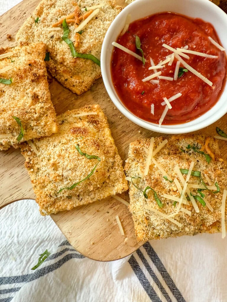 air fryer toasted ravioli on a wood tray with marinara sauce for dipping