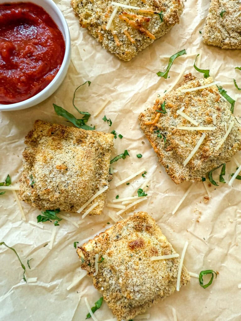 air fryer toasted ravioli on a parchment paper with marinara sauce for dipping