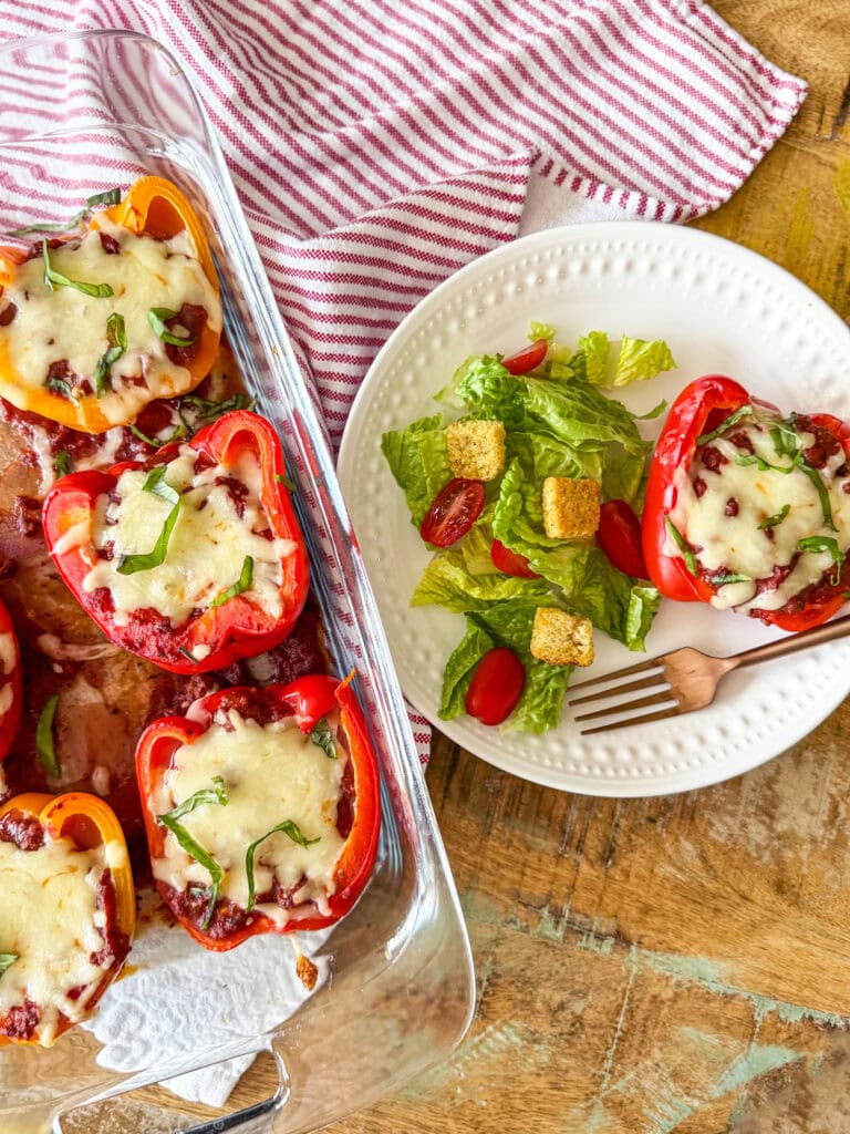 Italian Stuffed Pepper on a white plate with a side salad on top of a red and white striped napkin and a pan of baked stuffed peppers