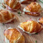 Mini Ham and Cheese Croissant Sandwiches on a wood tray with fresh herbs