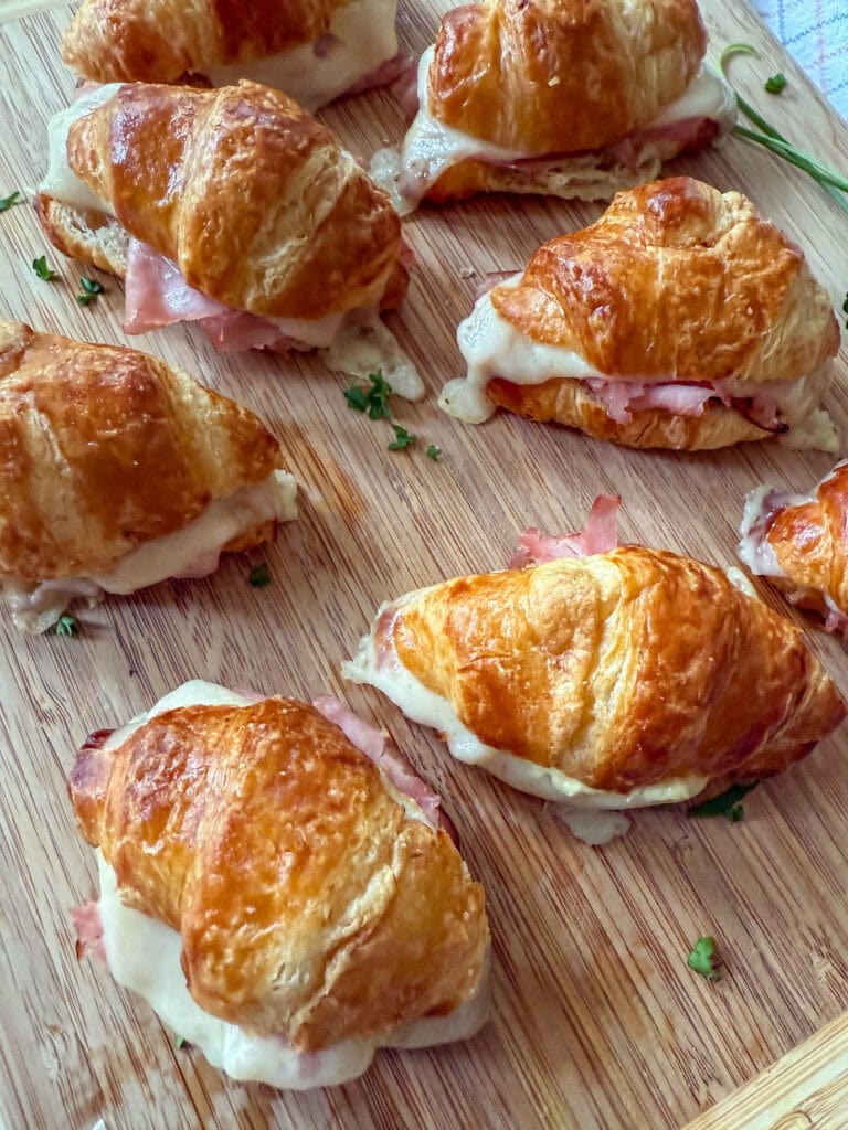 Mini Ham and Cheese Croissant Sandwiches on a wood tray with fresh herbs