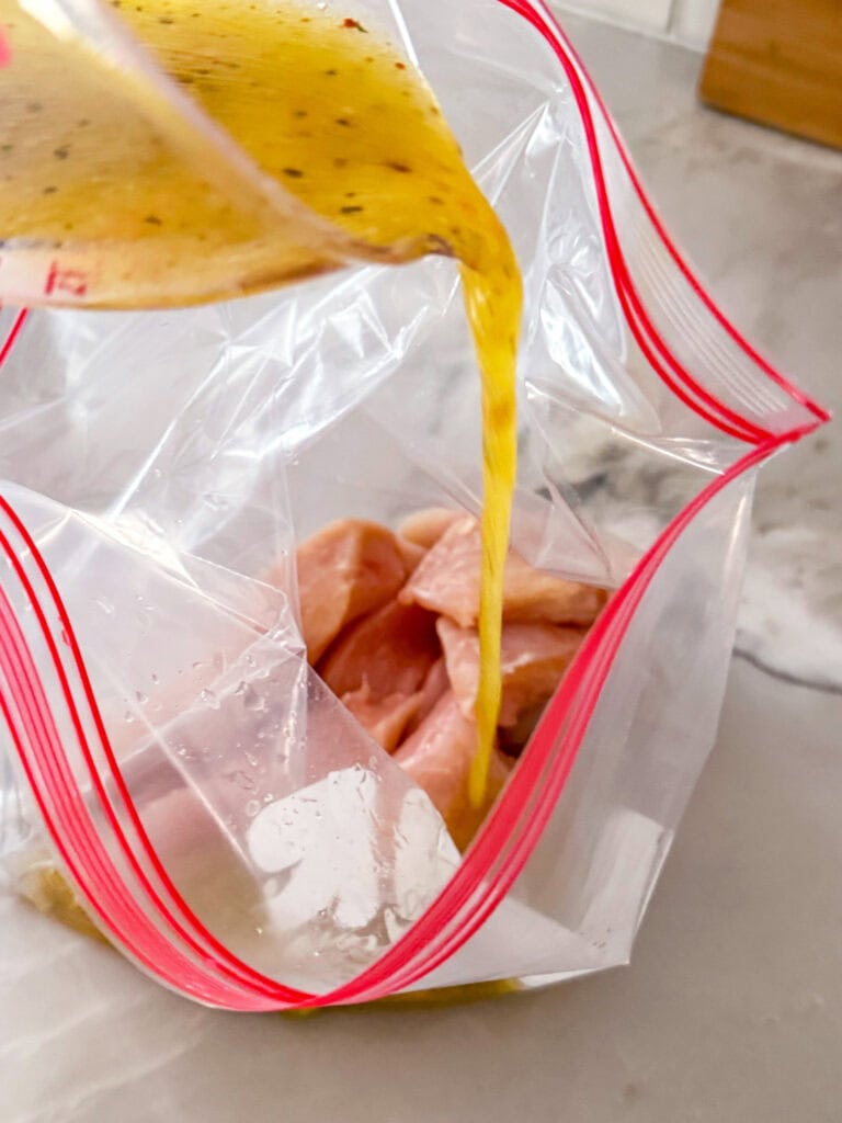 pouring Italian dressing into a bag of chicken for the marinade.