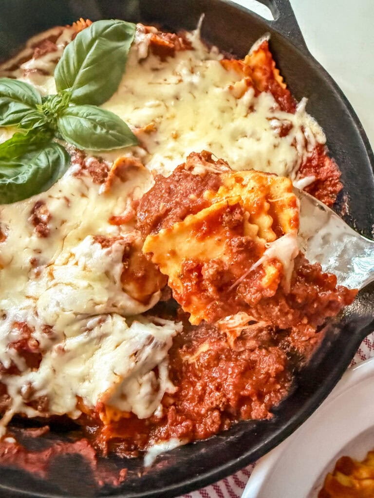 spooning a scoop of Skillet Ravioli with Meat Sauce on a red and white striped napkin
