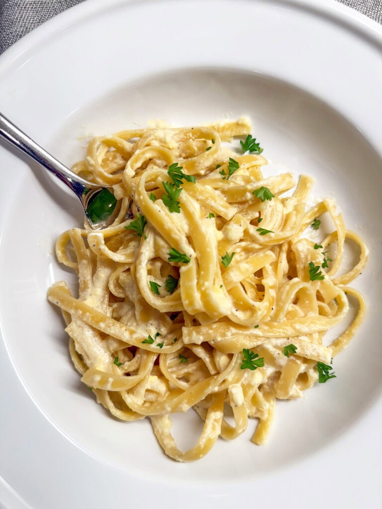 Close up of Copy Cat Olive Garden Fettuccine Alfredo in a white pasta bowl with a silver fork.