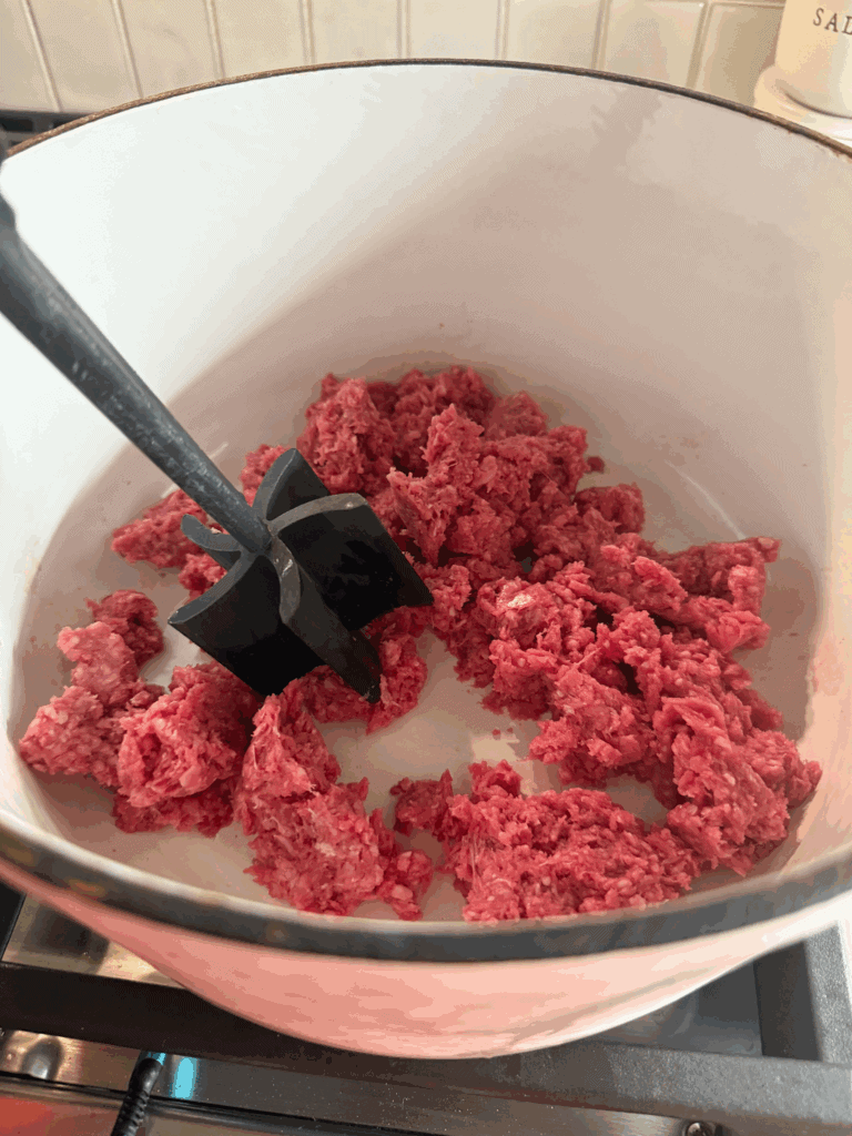 browning beef in large pot with a meat mashing tool