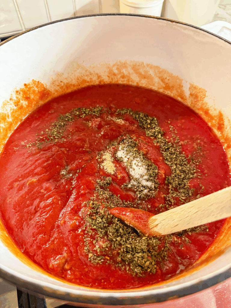 seasonings being stirred into meat sauce in a large white pot