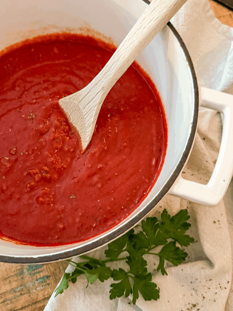 Homemade Italian Meat Sauce in a white pot with a wood spoon on a wood table