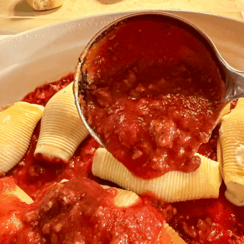 a ladle spooning Homemade Italian Meat Sauce over cheese stuffed pasta shells