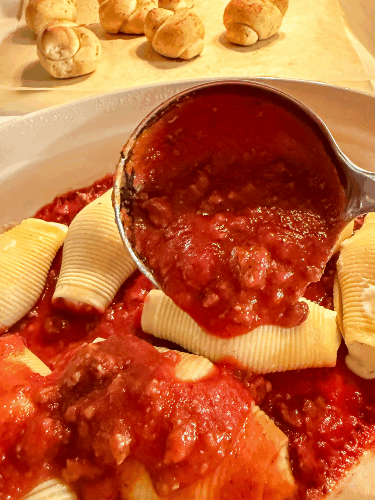 a ladle spooning Homemade Italian Meat Sauce over cheese stuffed pasta shells