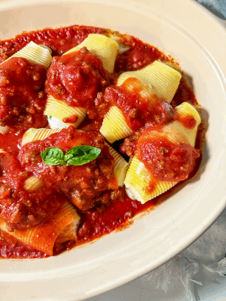 Homemade Italian Meat Sauce served over cheese stuffed pasta shells in a baking dish with basil garnish