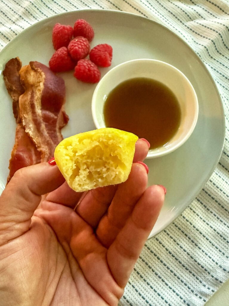 mini pancake bite with a bite out of it on a plate with bacon and berries and a side of maple syrup