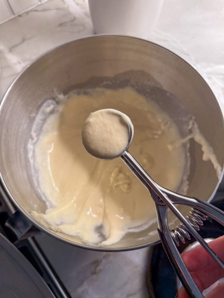 a small cookie scoop of pancake batter being held over bowl of batter