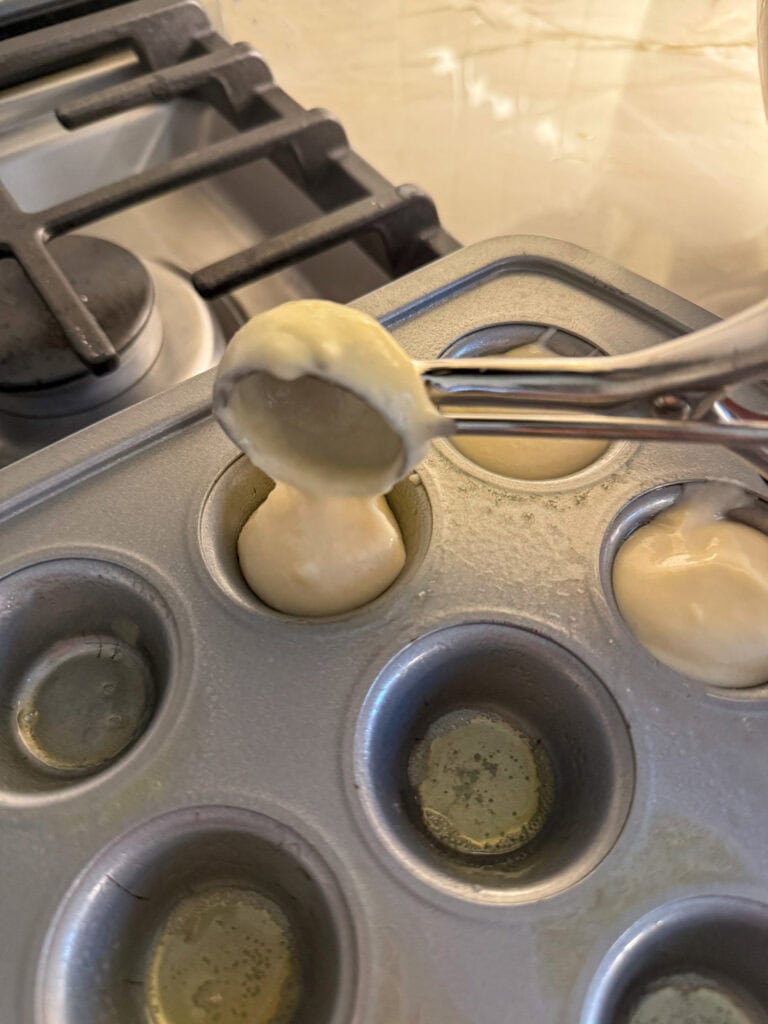 a cookie scoop adding batter to mini muffin tin