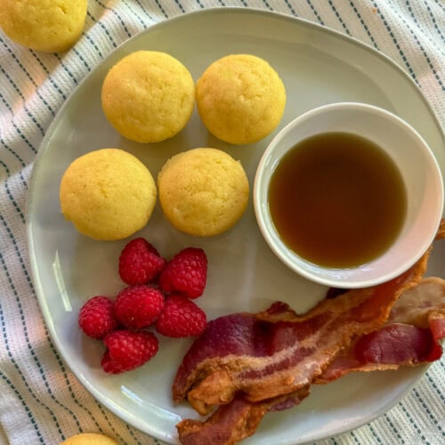 mini pancake bites on a plate with bacon and berries and a side of maple syrup