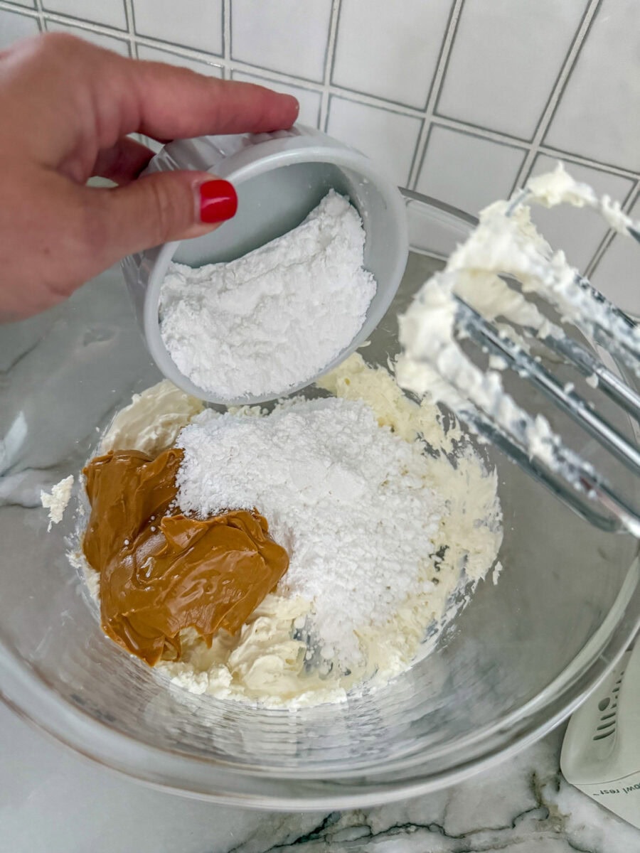 adding powdered sugar and peanut butter to the Reese's Peanut Butter Cup Dip mixture in a large glass bowl