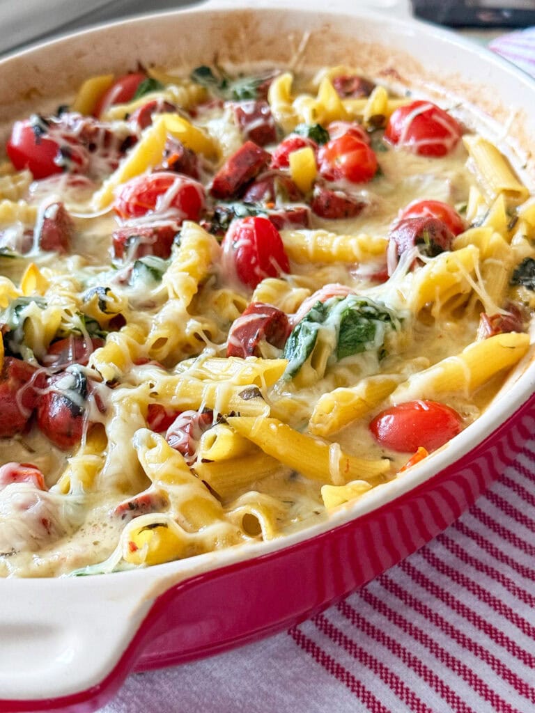 Spinach and Artichoke Dip Pasta Bake with Chicken Sausage in a red baking dish with a red and white stripped napkin
