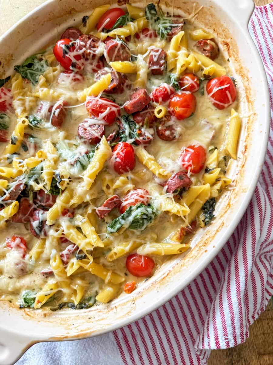 Spinach and Artichoke Dip Pasta Bake with Chicken Sausage in a red baking dish with a red and white stripped napkin