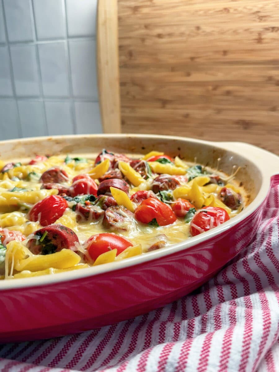the viral recipe of Spinach and Artichoke Dip Pasta Bake with Chicken Sausage in a red baking dish with a red and white stripped napkin