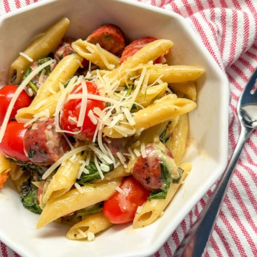 Spinach and Artichoke Dip Pasta Bake with Chicken Sausage served in aa white dish with a red and white stripped napkin and fork
