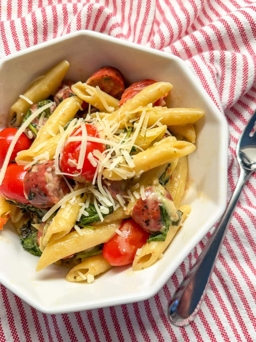 Spinach and Artichoke Dip Pasta Bake with Chicken Sausage served in aa white dish with a red and white stripped napkin and fork