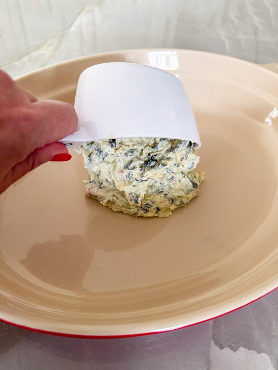 scooping spinach and artichoke dip into baking pan