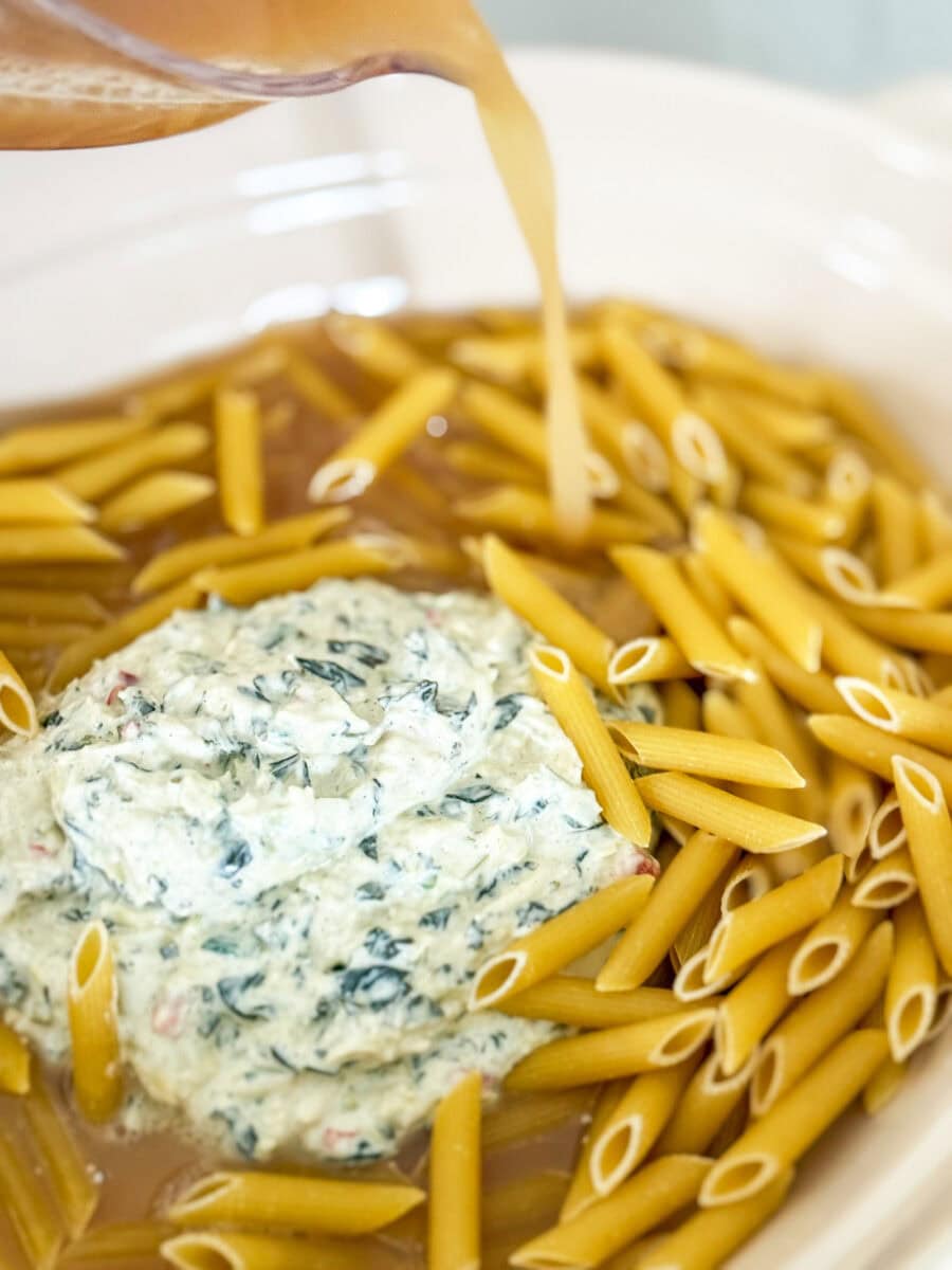 pouring chicken broth over dry pasta in dish with dip