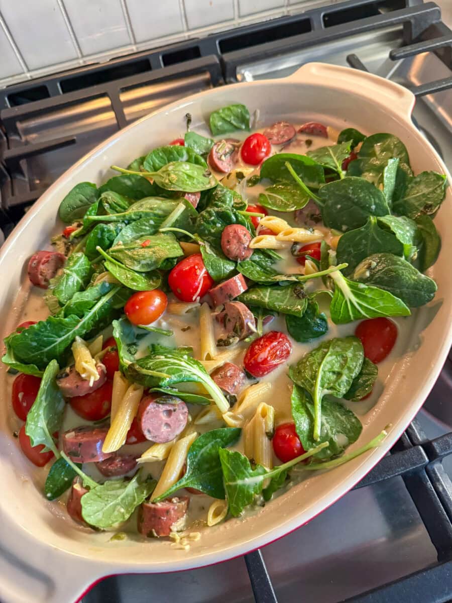 adding fresh spinach to Spinach and Artichoke Dip Pasta Bake with Chicken Sausage