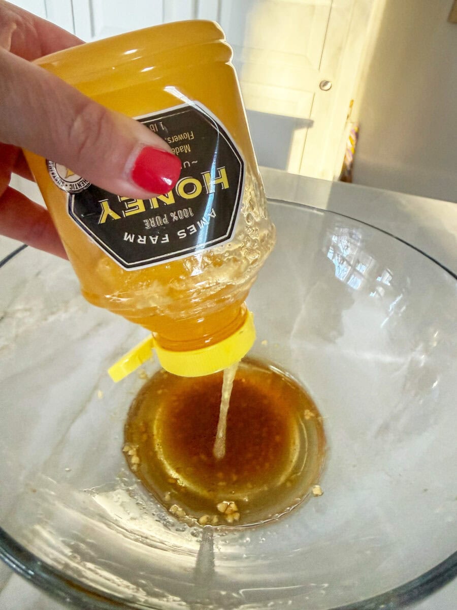 pouring honey into a large glass bowl to make the dressing for Asian Chicken Wraps