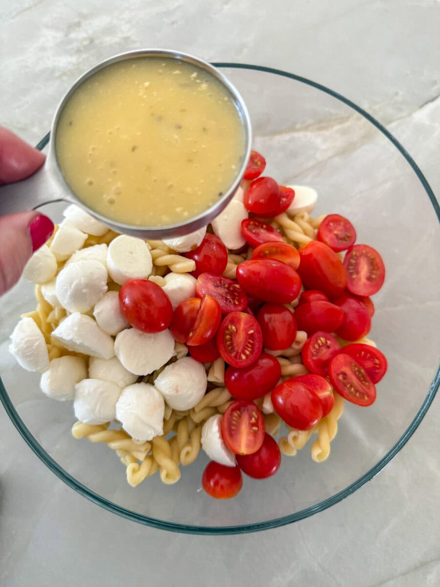 adding Italian dressing to bowl of mozzarella, tomatoes and cooked pasta