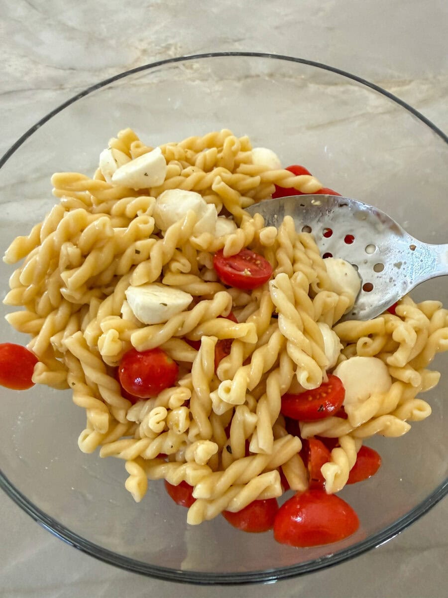 tossing Caprese Pasta Salad in a glass bowl