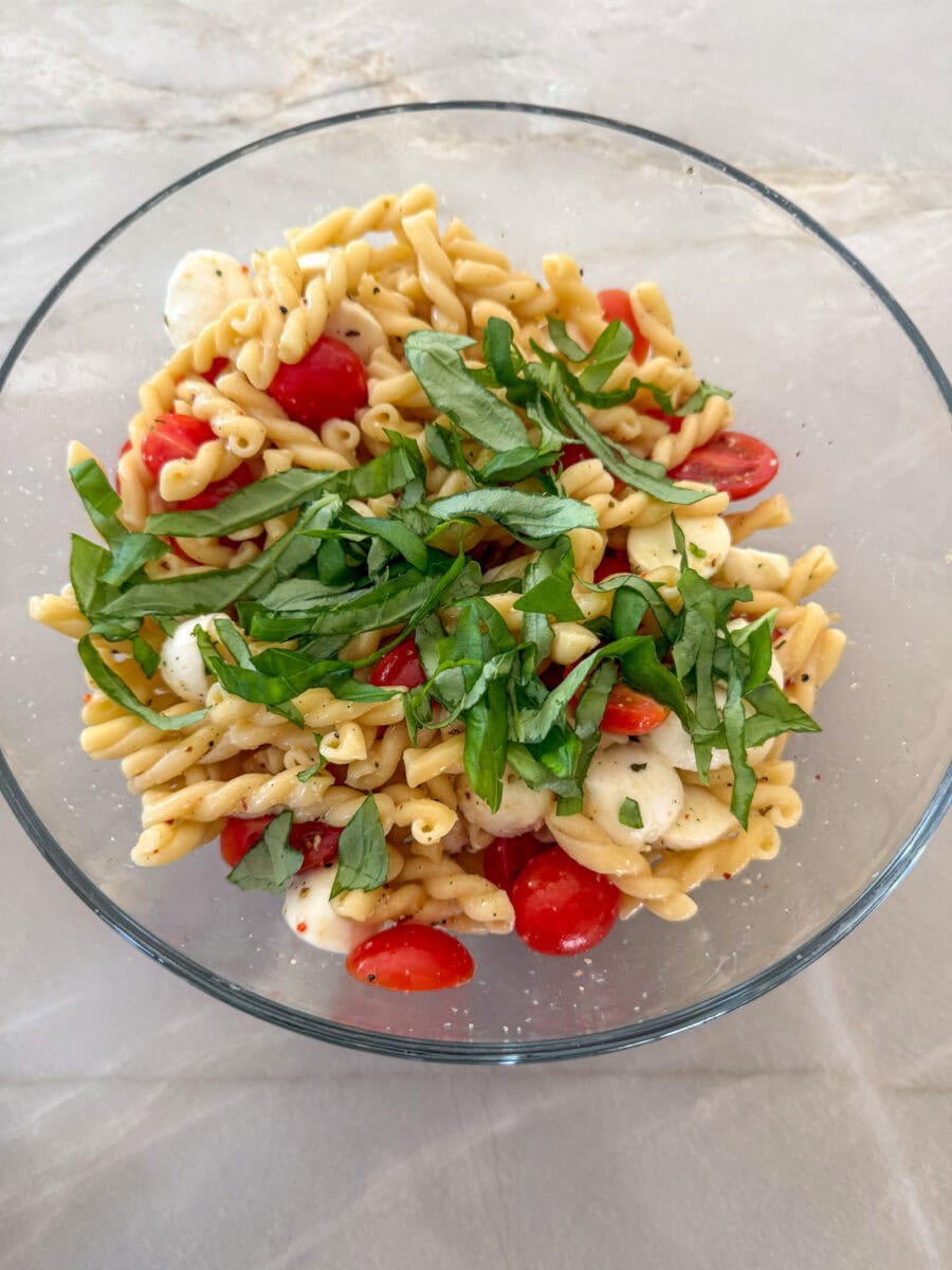 Caprese Pasta Salad in a glass bowl ready to be tossed with fresh basil