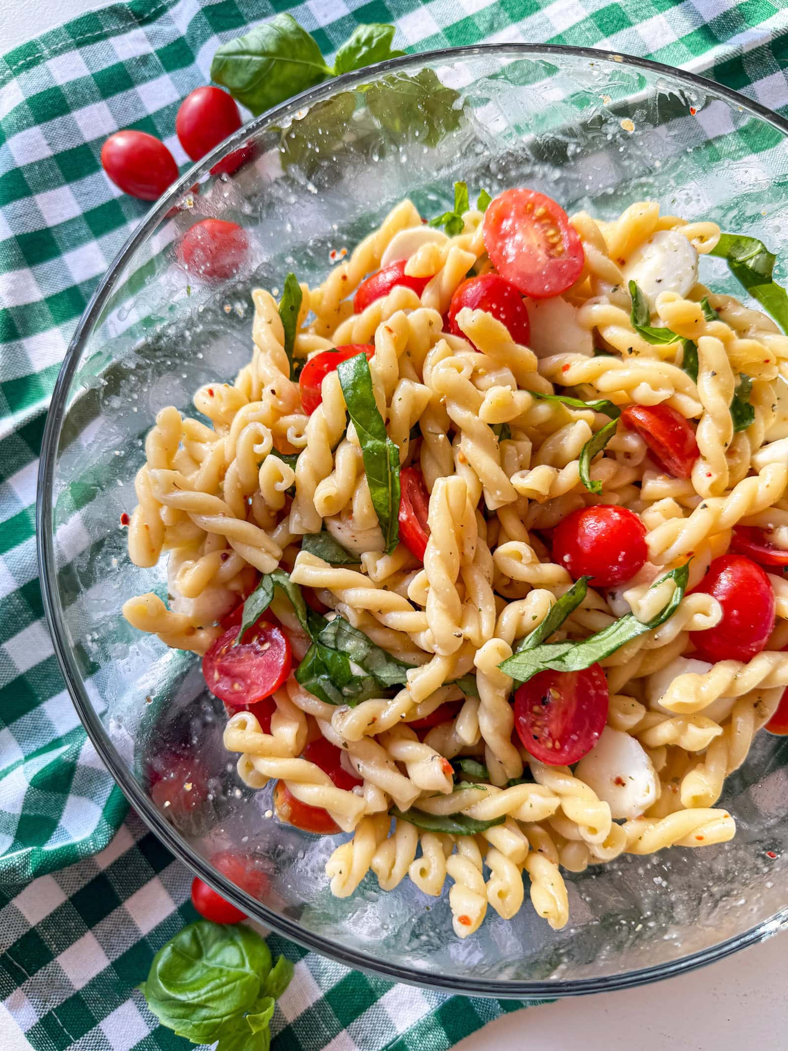 Caprese Pasta Salad in a glass bowl on a green and white check napkin