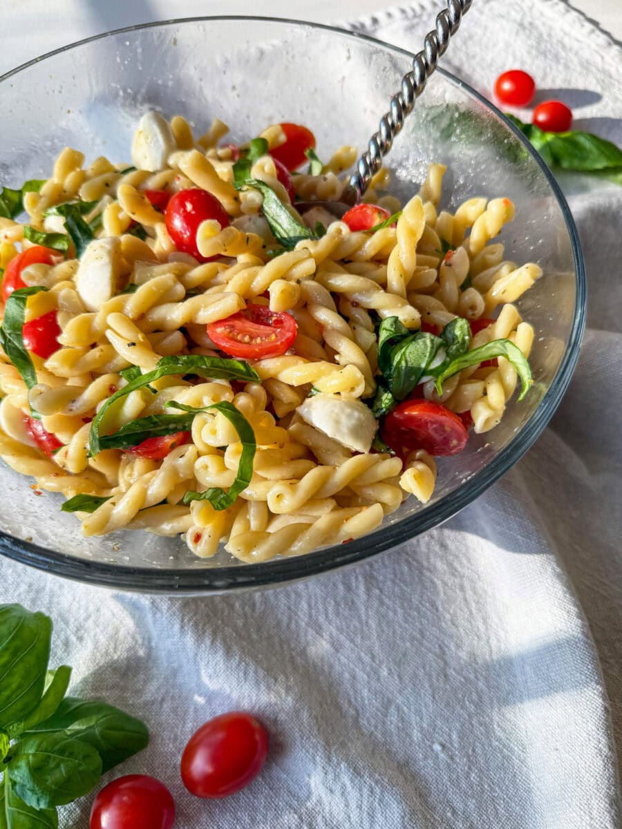 Caprese Pasta Salad in a glass bowl with a silver spoon on a grey napkin