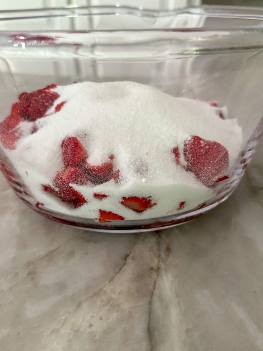 Sugar and strawberries in a large glass mixing bowl
