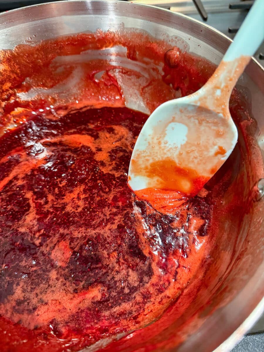 skimming foam of top of cooked jam in saucepan for homemade strawberry jam