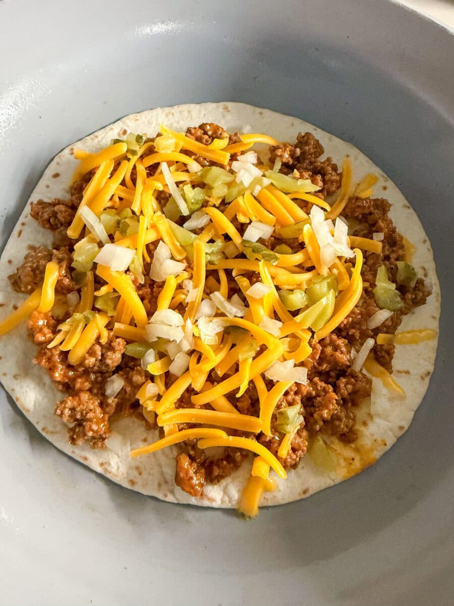loading quesadilla with burger toppings in fry pan
